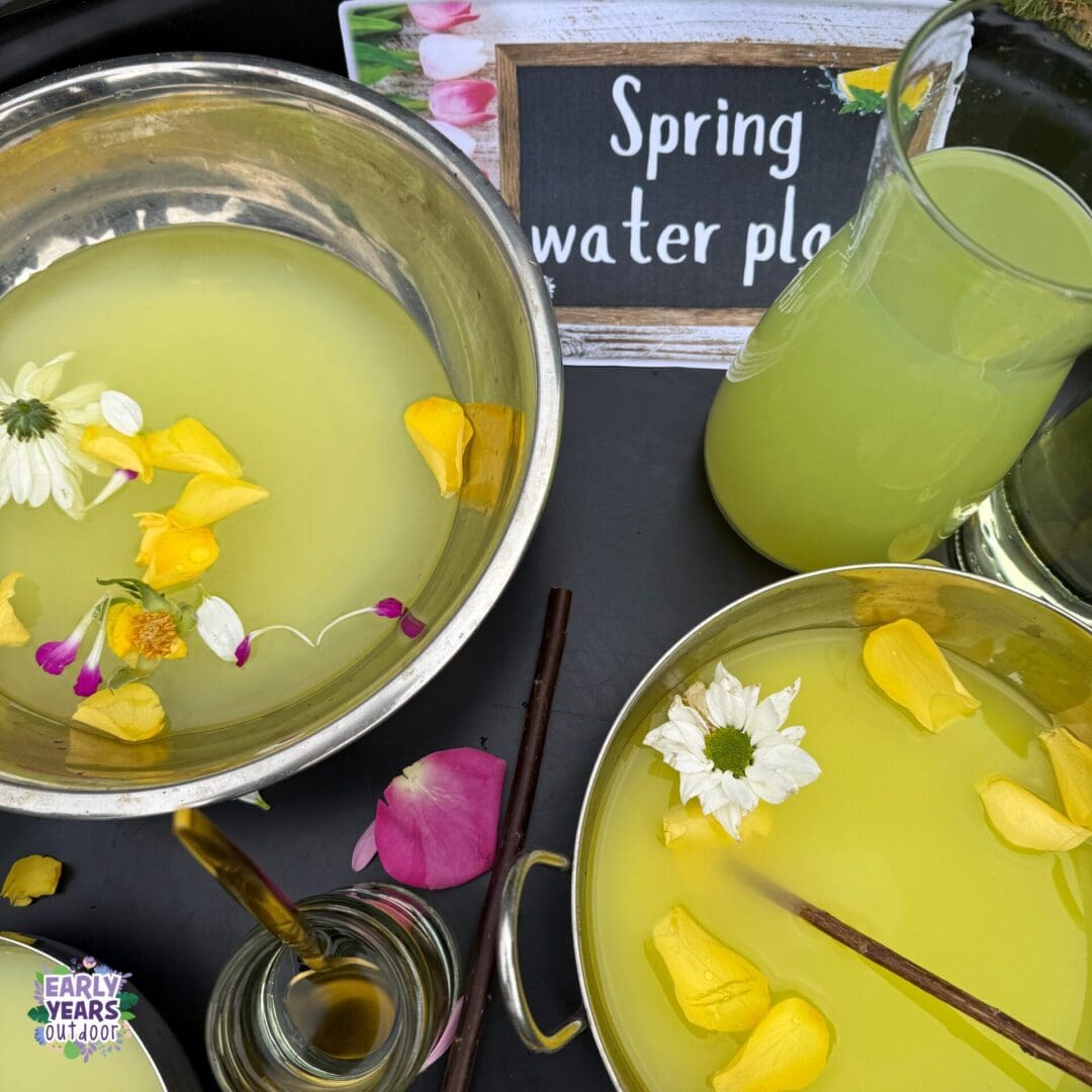 Spring water play activity Spring water play tuff tray set up with sign, bowls of yellow water with petals and flowers, jugs, jars and sticks